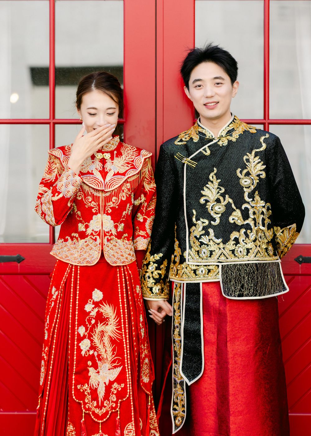 Couple in traditional Chinese wedding attire, bride in red and gold hanfu, groom in black and gold tang suit.