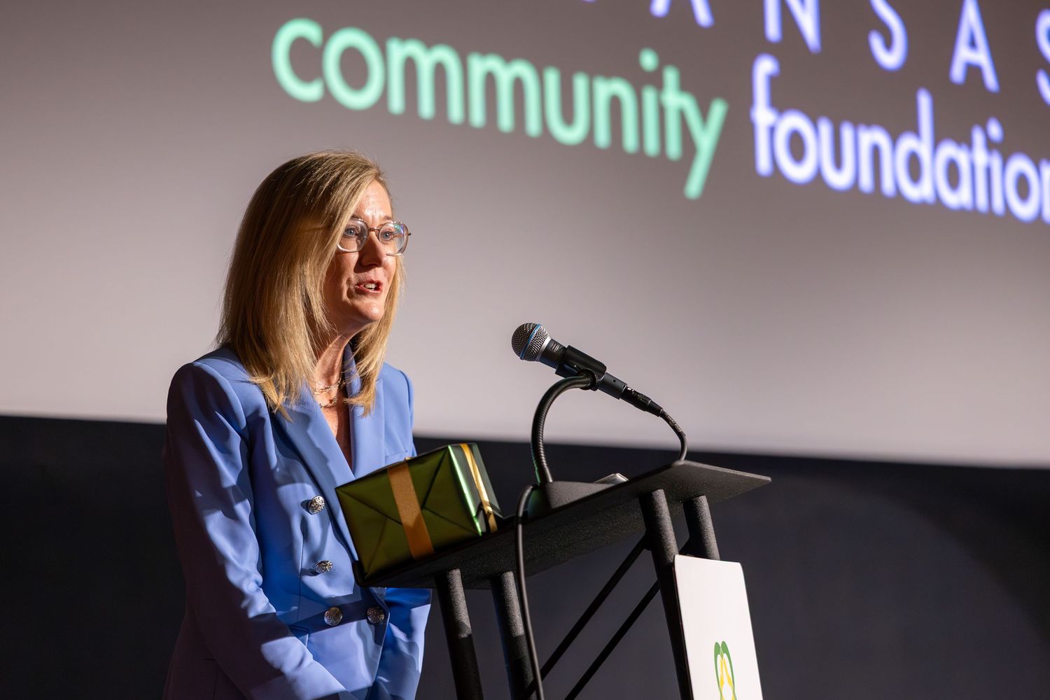 Woman speaking at podium during Kansas Community Foundation event on stage with microphone.