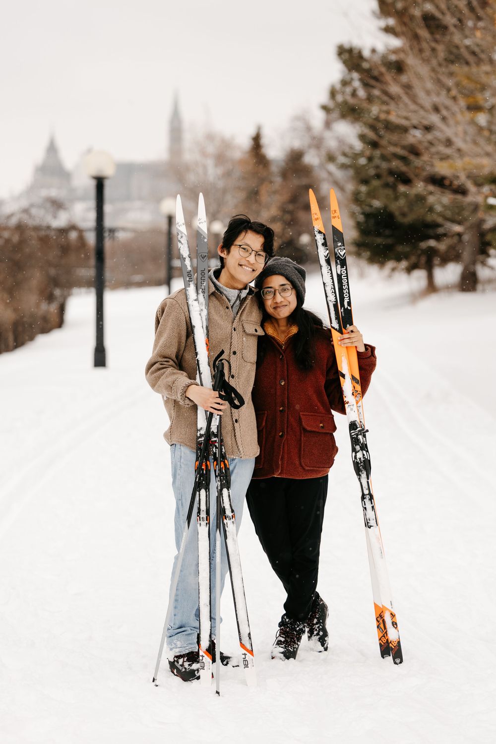 Young couple holding cross-country skis together on snowy trail in winter park.