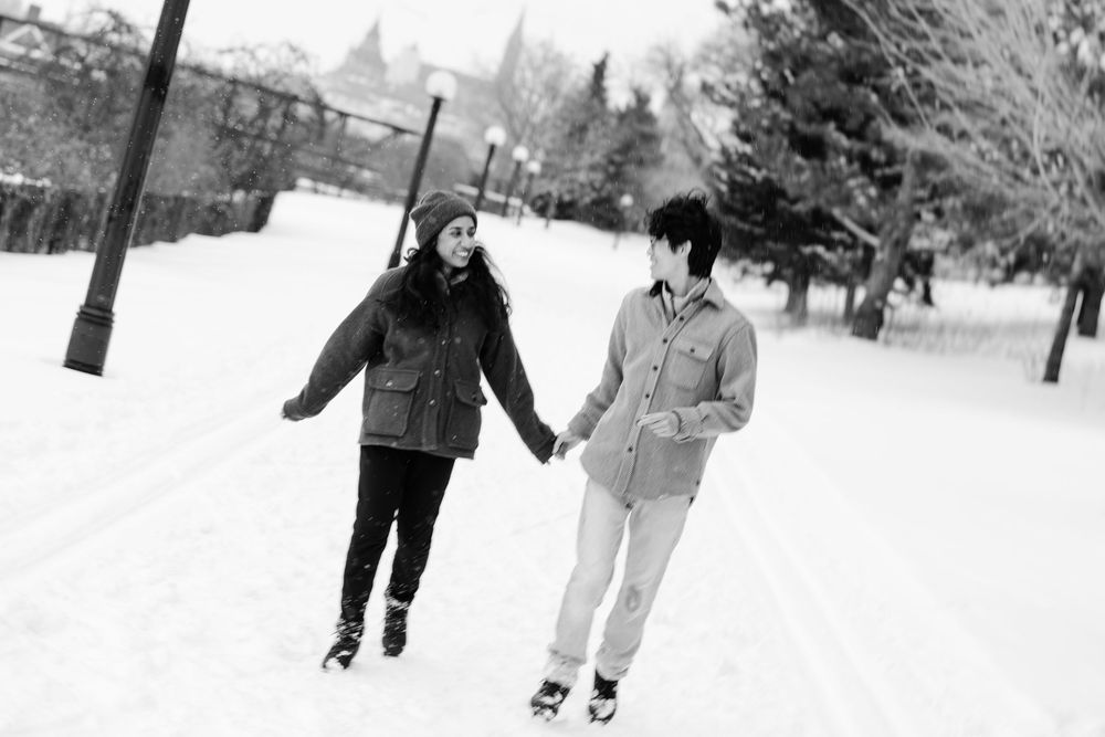 Couple holding hands ice skating on snowy path in black and white winter photo.