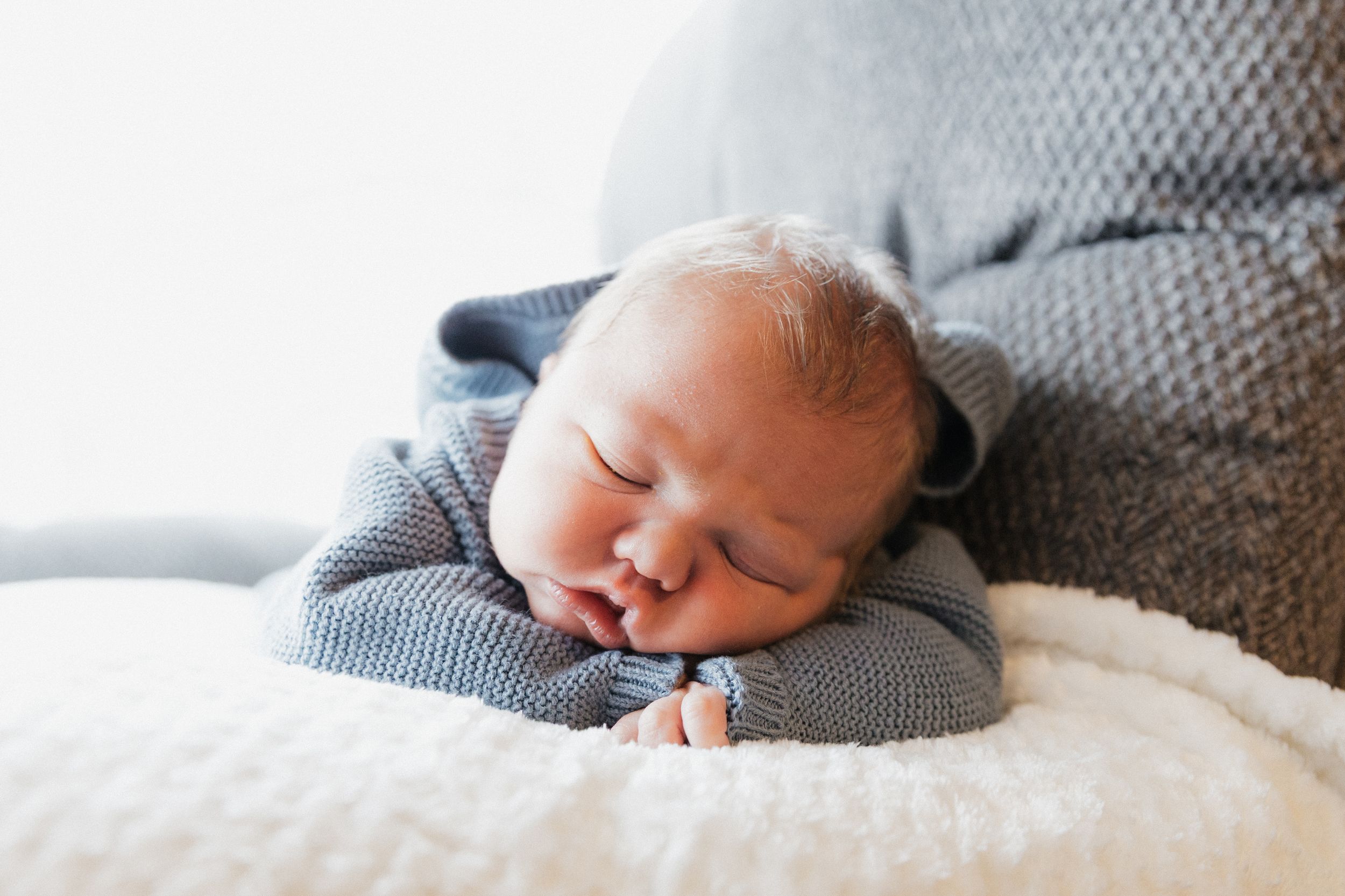 Peaceful newborn baby sleeping on a fluffy white blanket wearing a soft blue knit outfit.