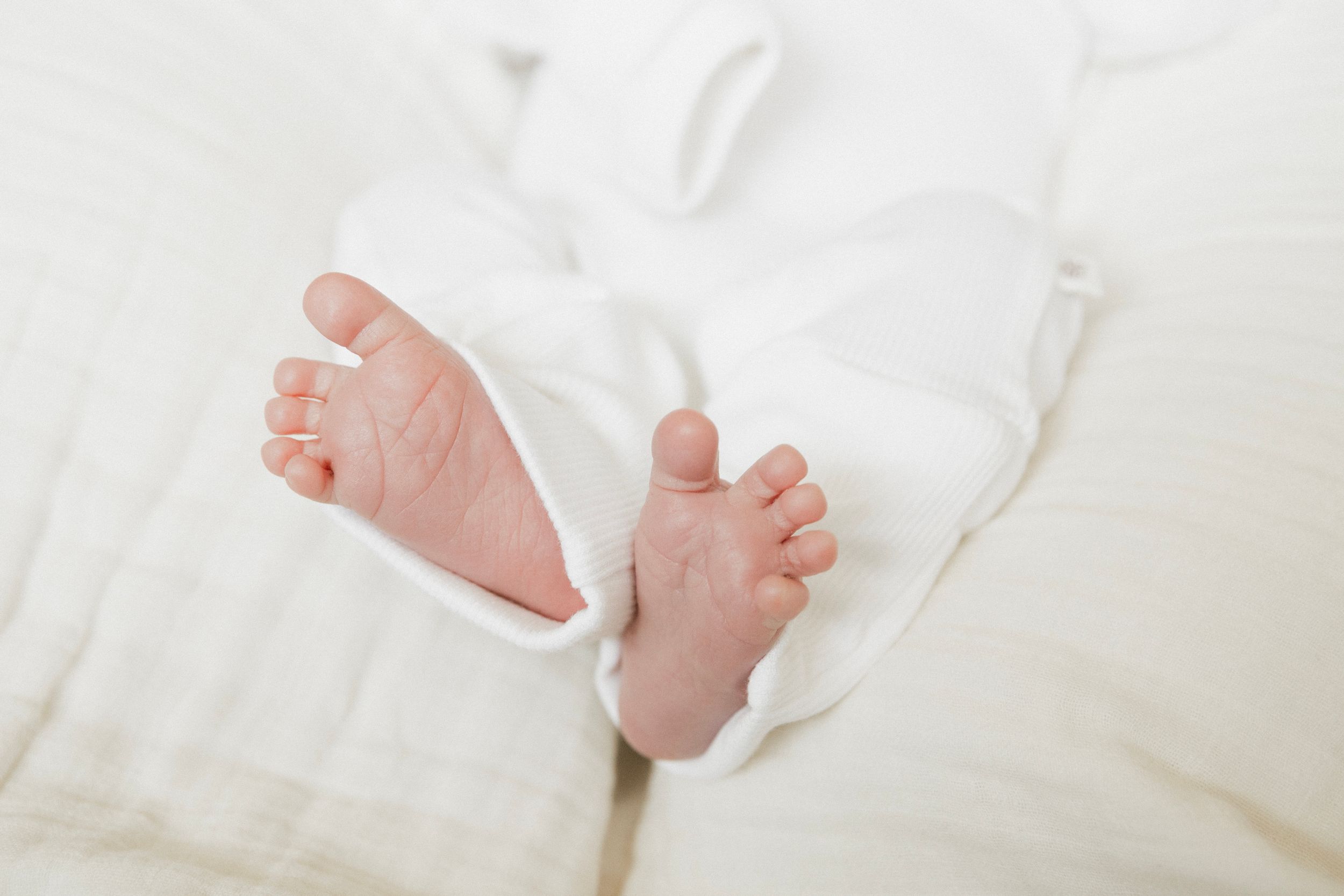 Close-up of newborn baby feet wrapped in soft white blanket on white bedding.