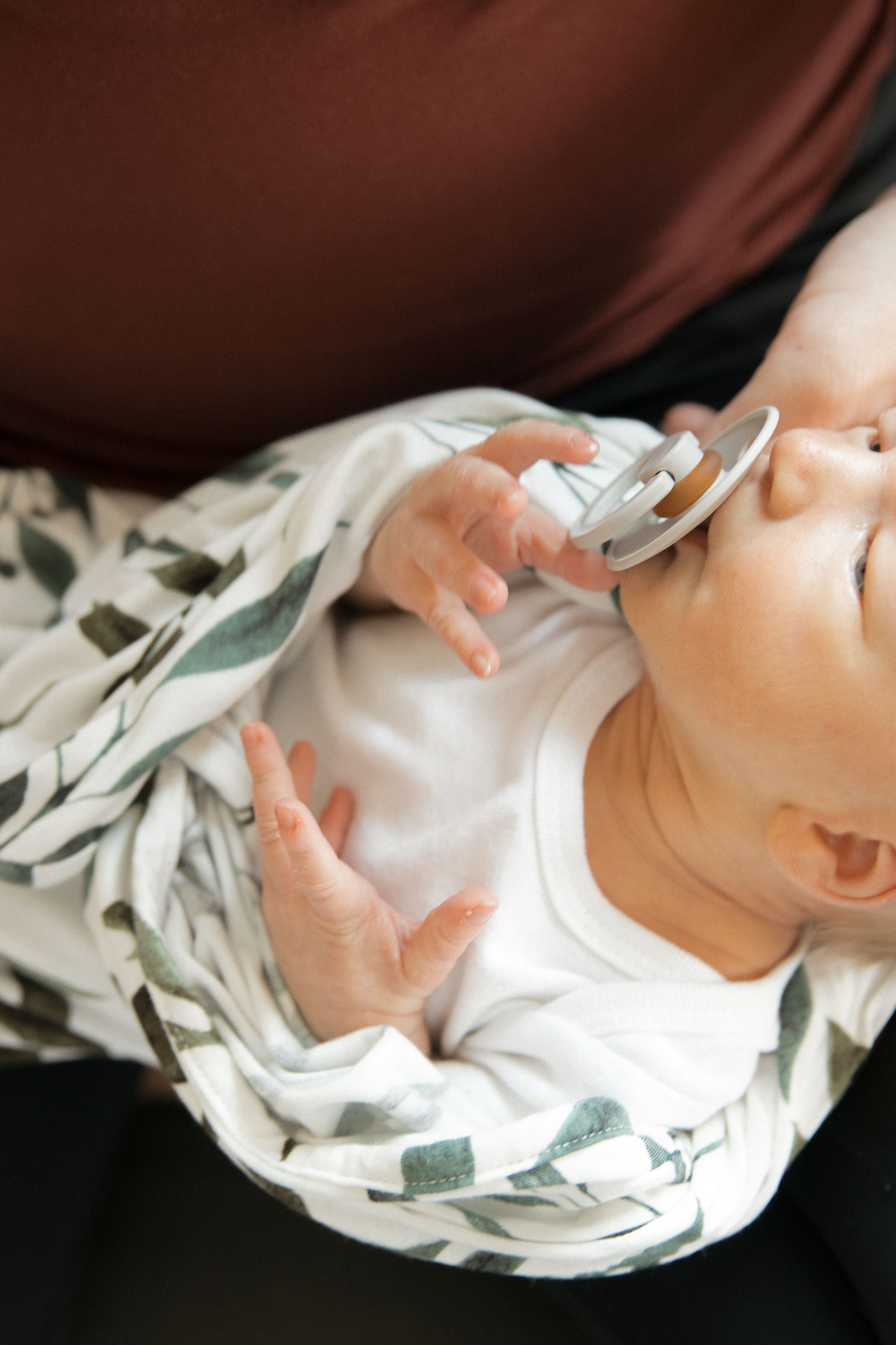 A peaceful baby with a pacifier rests in a caregiver's arms, wrapped in a soft floral swaddle blanket.