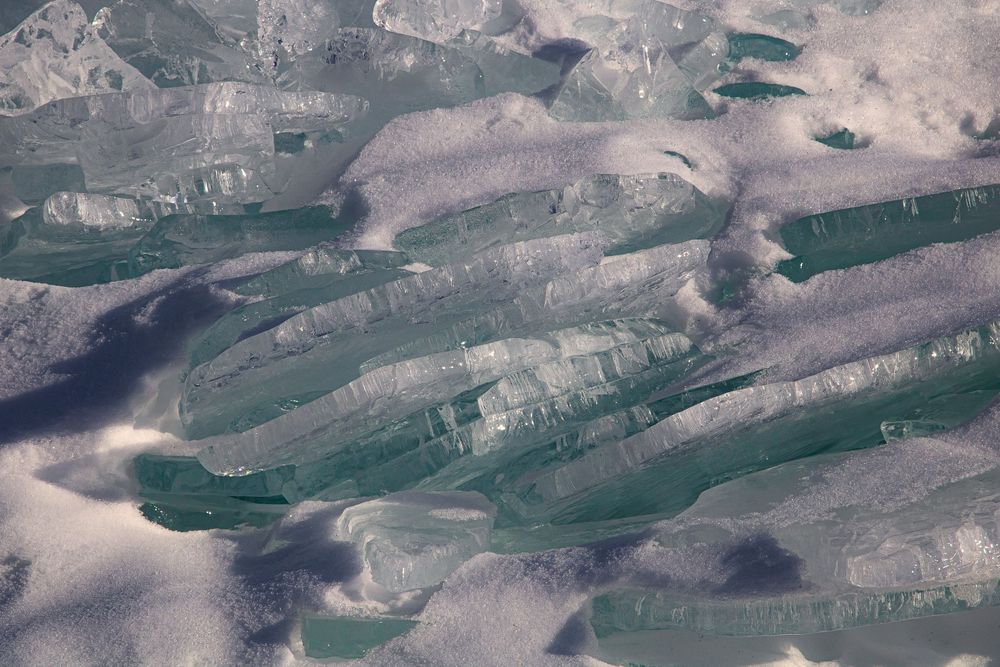 Close-up of translucent green and purple ice formations layered together on a frozen surface.