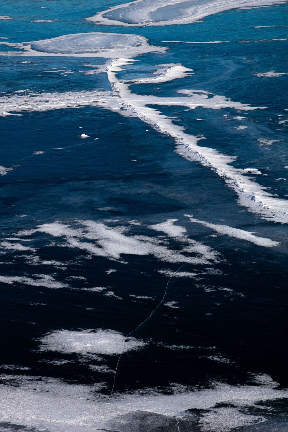 Aerial view of a partially frozen lake with ice formations and dark blue water creating abstract winter patterns.
