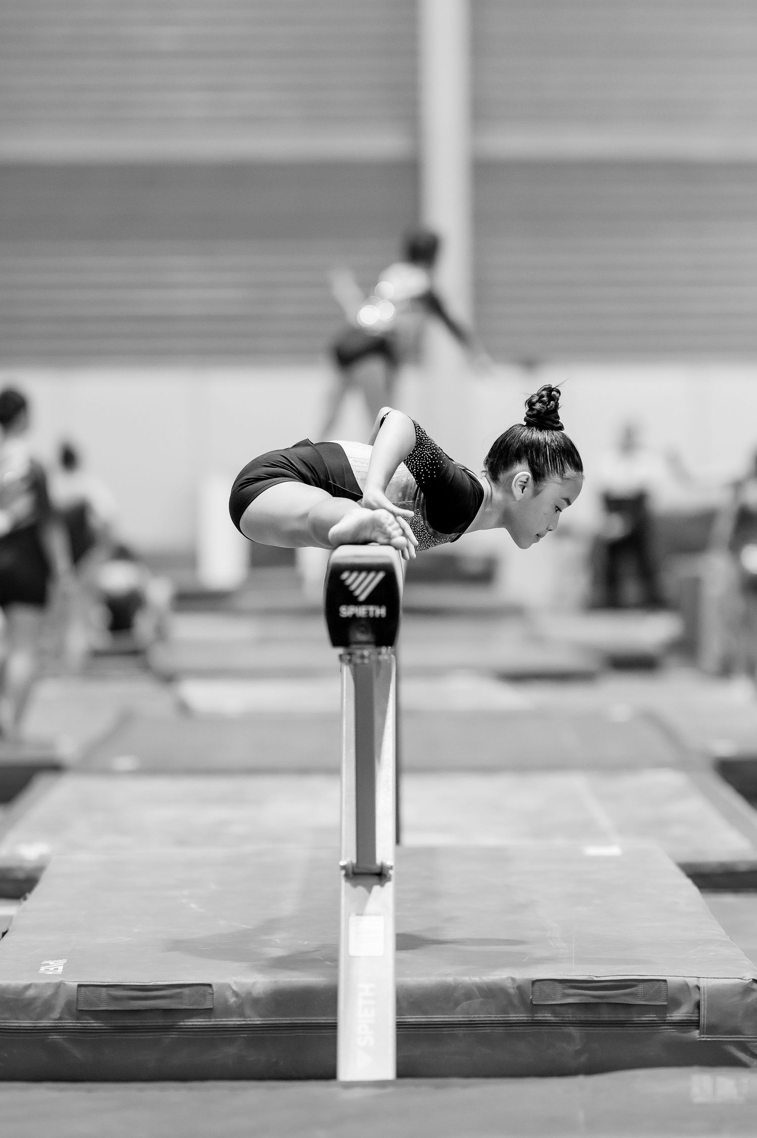 Young gymnast performs a balance skill on a Spieth apparatus in an indoor gymnastics training facility with blue and red mats.