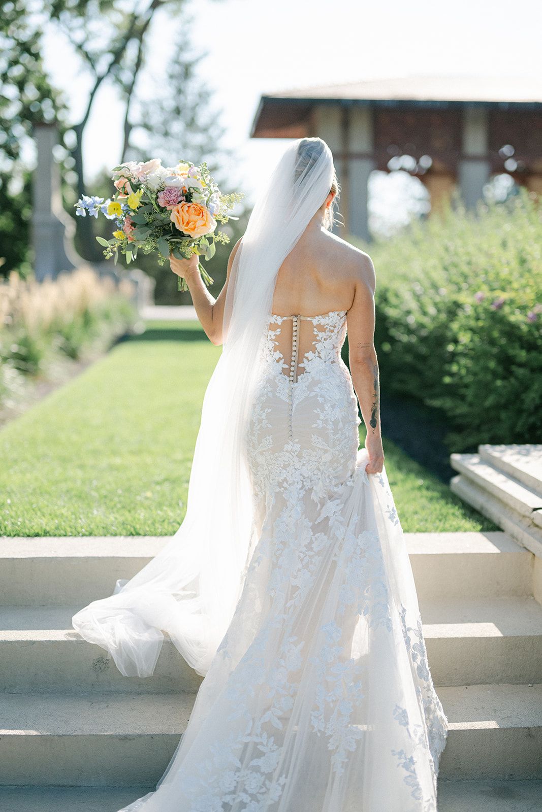 Armour House Wedding - Bride in lace gown holds colorful bouquet flanked by bridesmaids in sage floral dresses at wedding.