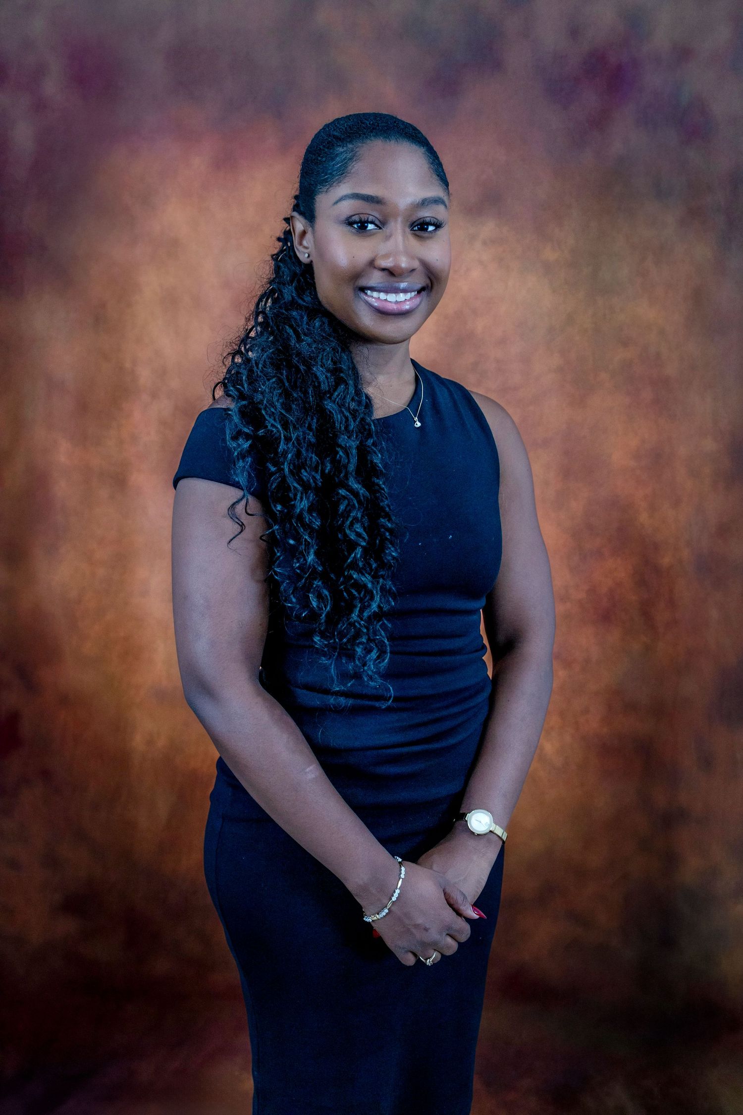 on location photobooth Smiling young woman with long curly hair wearing a navy dress and watch, posing for a professional portrait photo.