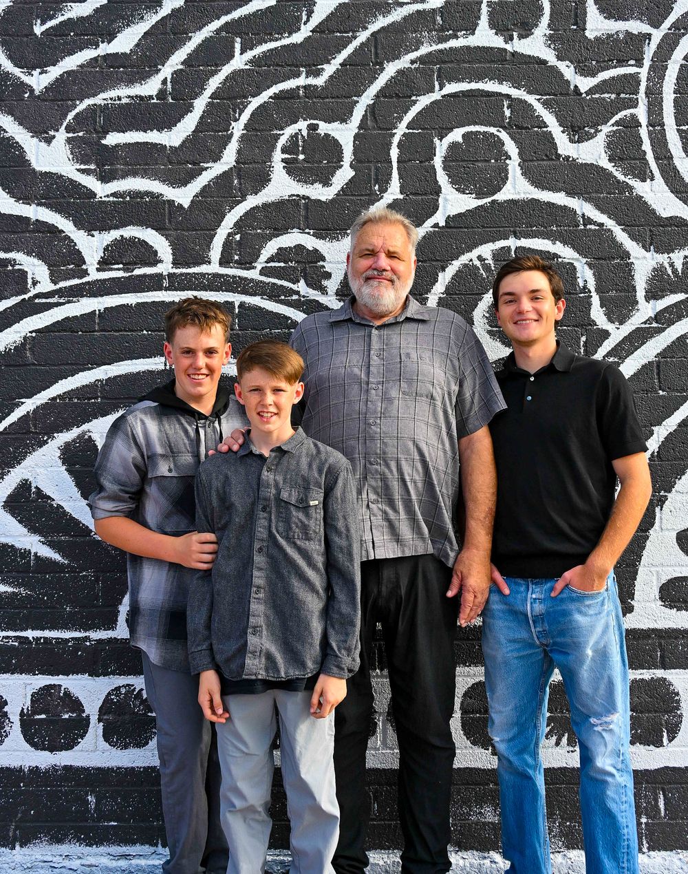 Older man posing with three boys in front of black and white geometric mural.