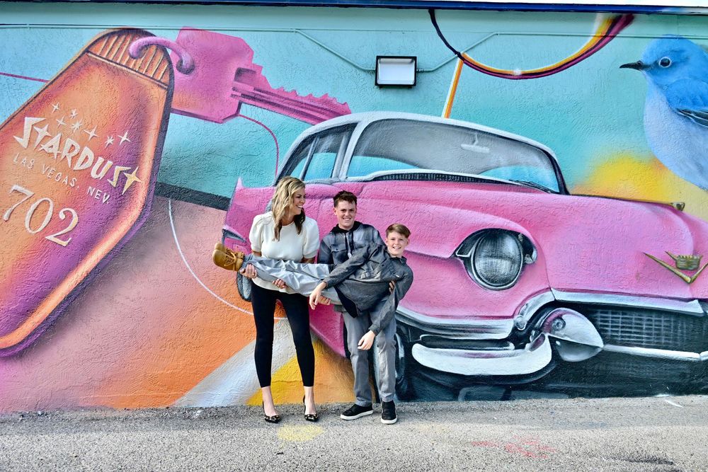 Couple posing in front of a colorful Las Vegas Stardust Hotel mural featuring a pink Cadillac.