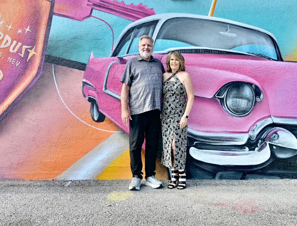 Couple posing in front of a colorful pink classic car mural on a vibrant street art wall.