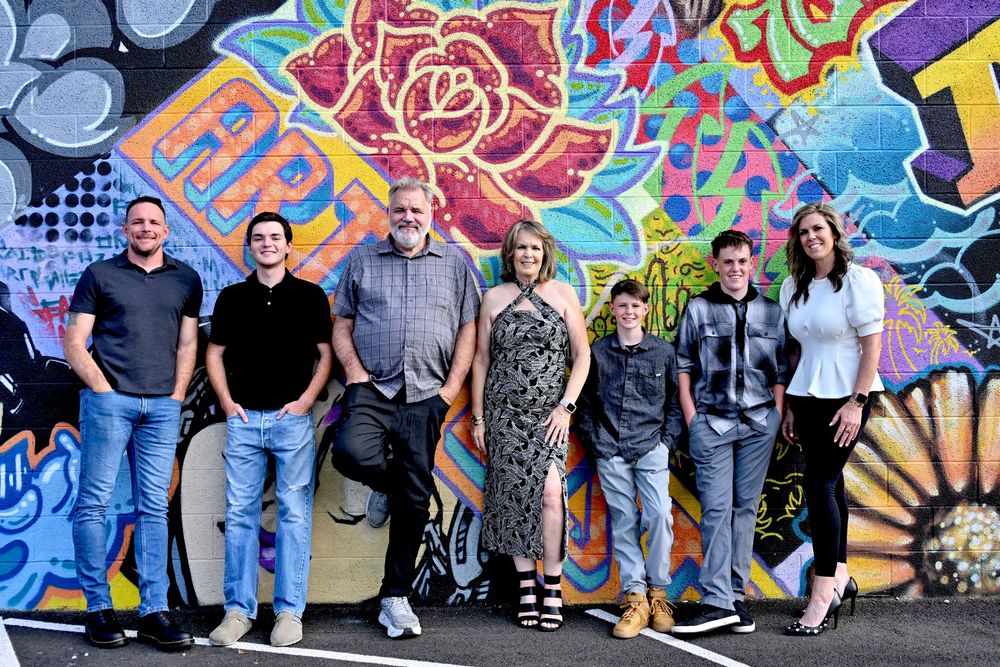 Group of seven people posing together in front of a vibrant colorful graffiti mural wall.