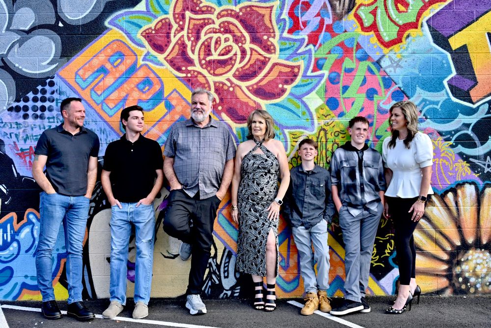 Group of seven people smiling in front of a vibrant floral graffiti wall mural.