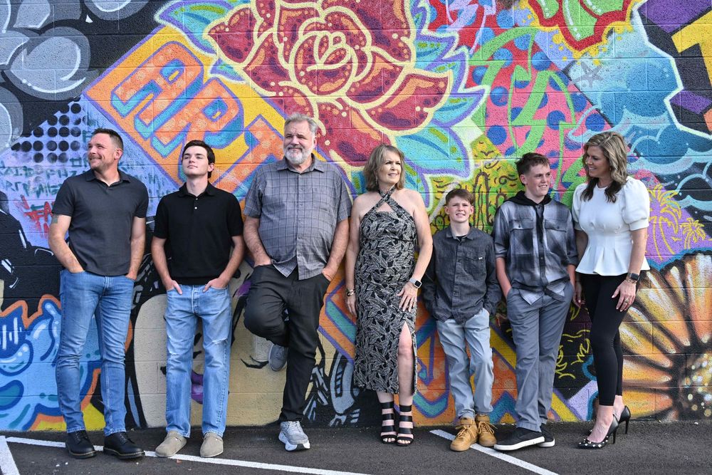 Group of seven people posing together in front of a vibrant colorful floral graffiti mural wall.