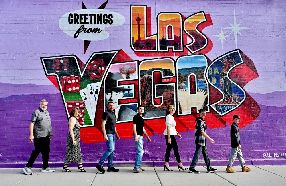 Group of people walking in front of a large Greetings from Las Vegas street mural.