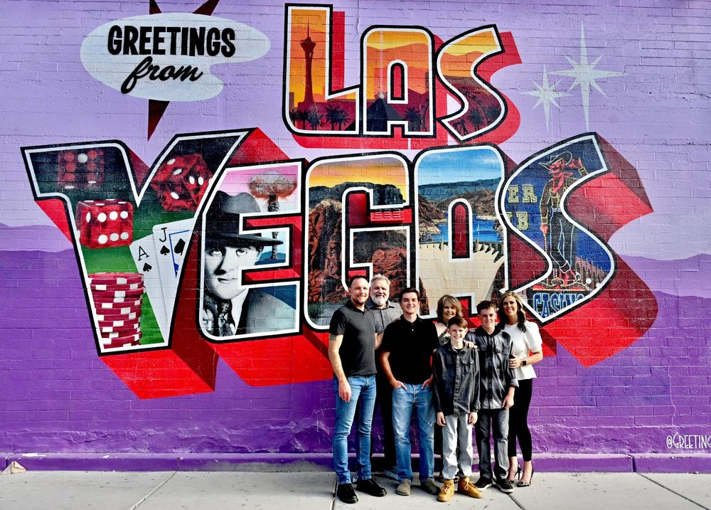 Group of five people posing in front of a vibrant Greetings from Las Vegas mural.