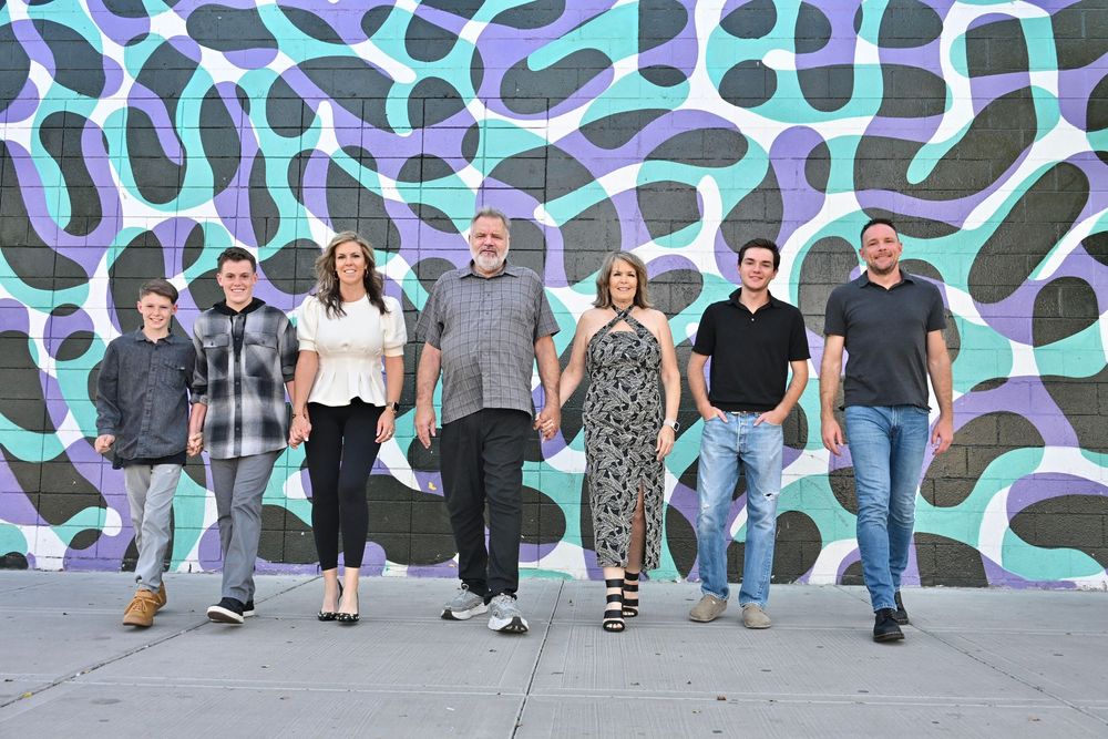 Group of seven people smiling and holding hands in front of a vibrant blue and black abstract mural.