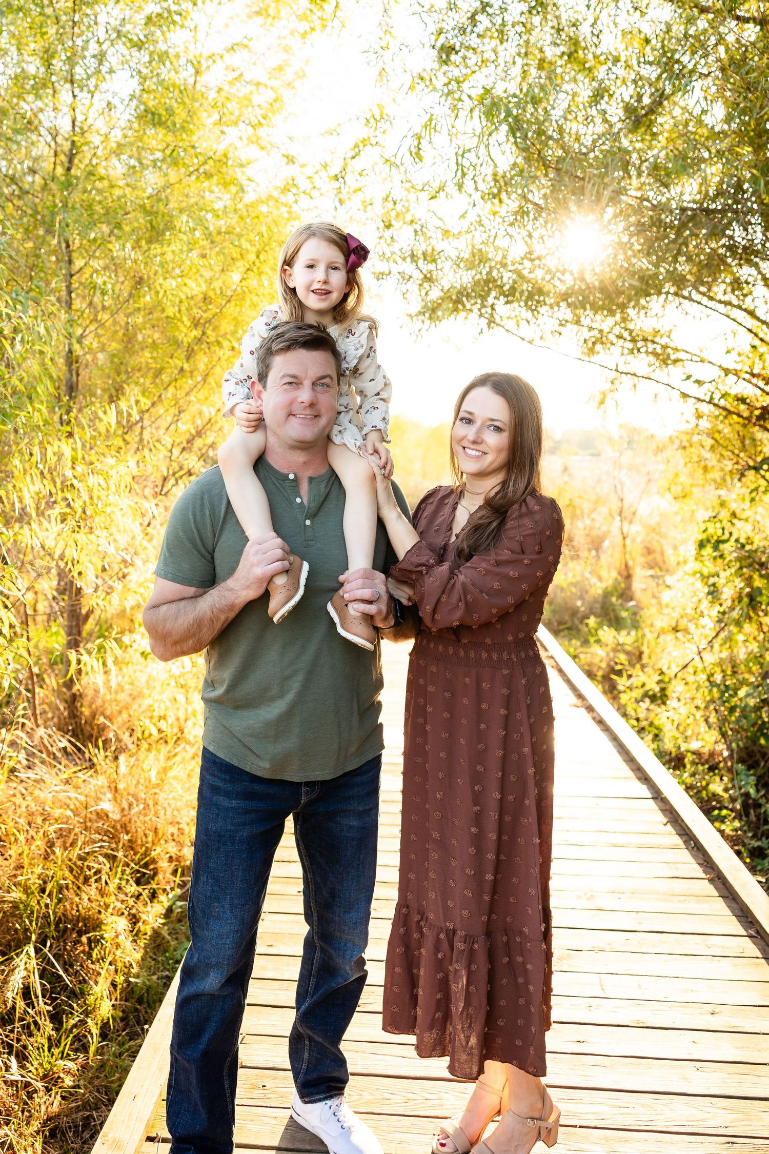 A couple shares playful moments on a wooden boardwalk surrounded by golden autumn foliage during sunset.