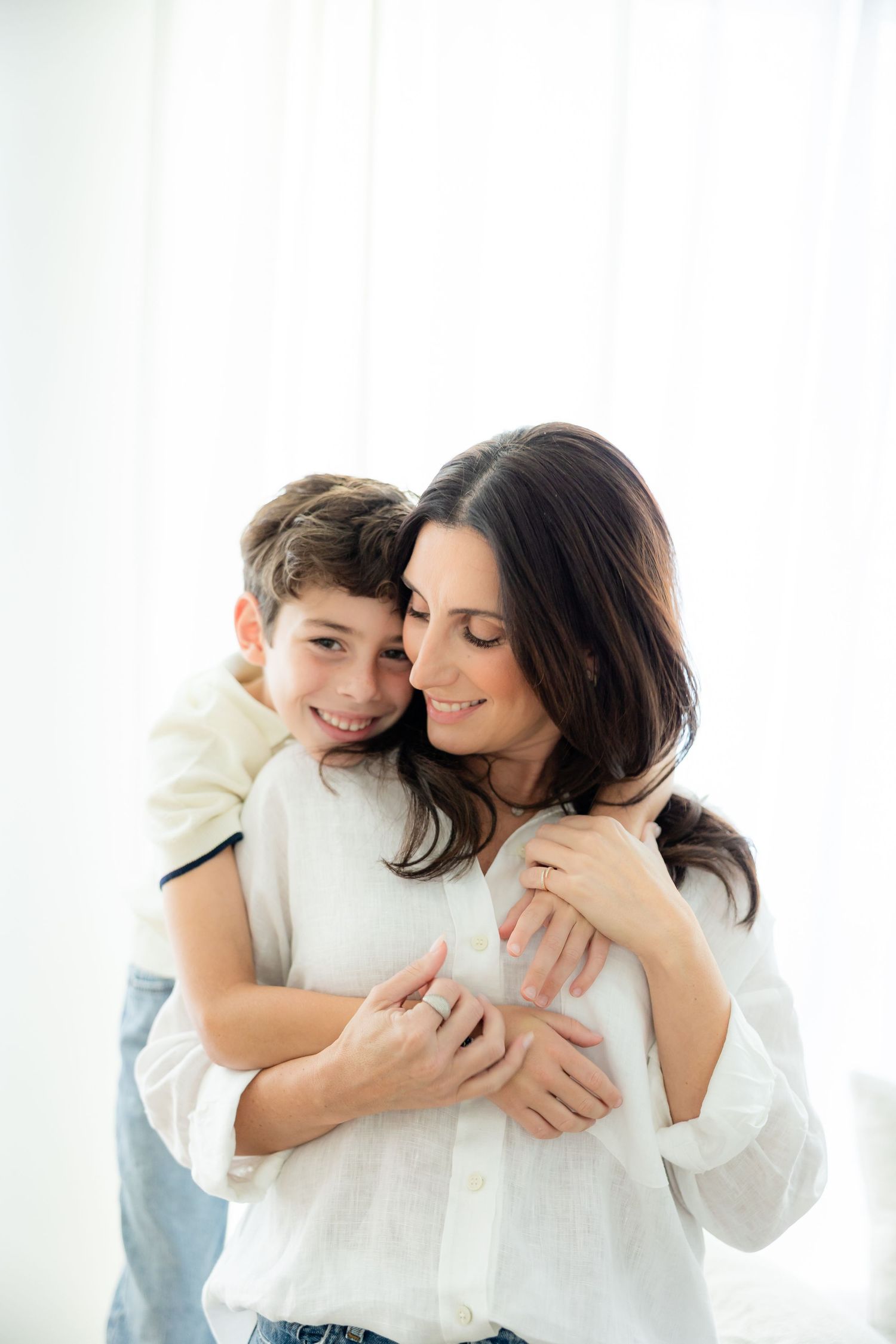 A tender moment shared between parent and child hugging and smiling together against a bright white background.
