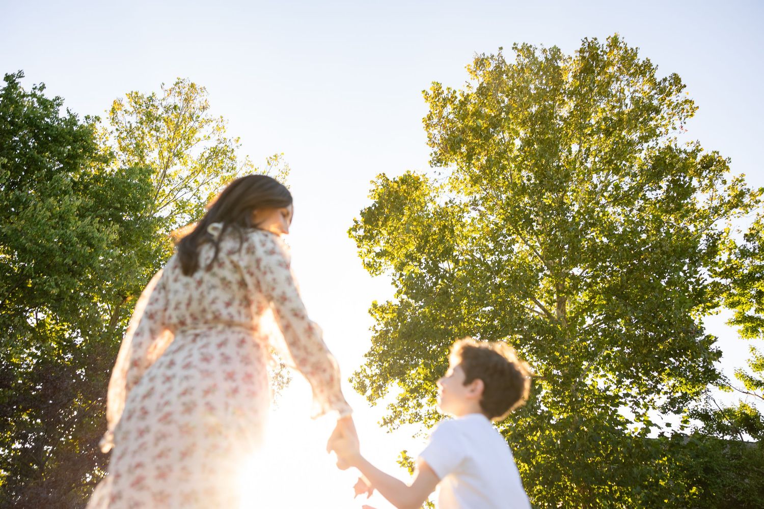 Silhouettes of people dancing and jumping in a park during golden hour with sunlight streaming through trees.