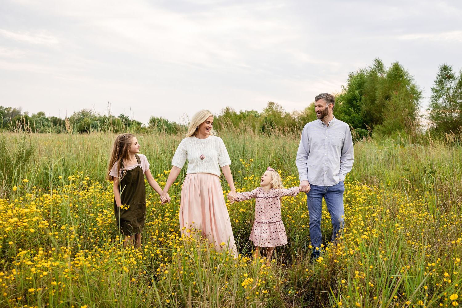 People walking through a vibrant summer meadow filled with yellow wildflowers and green grass.