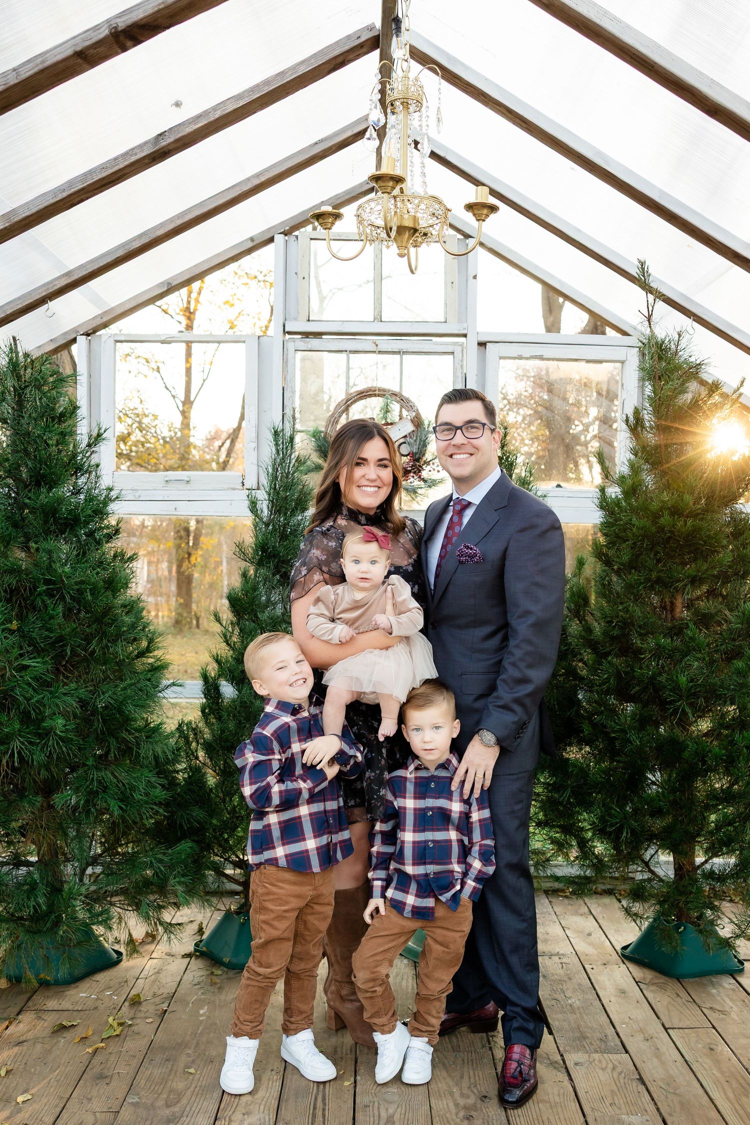 Family poses together in a greenhouse with evergreen trees during a winter photo session.