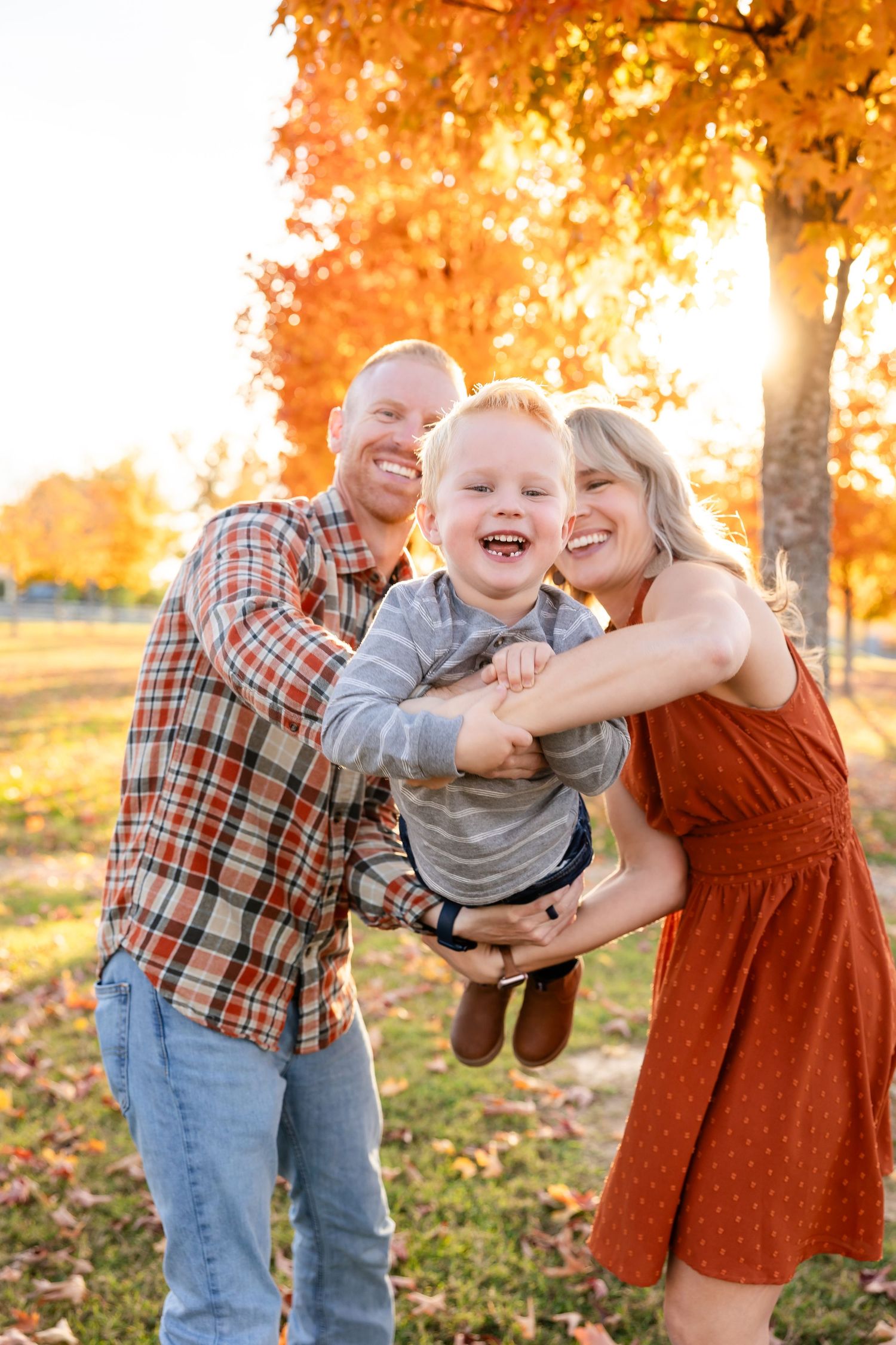 A joyful autumn family photoshoot in a park with golden leaves and warm sunlight filtering through the trees.