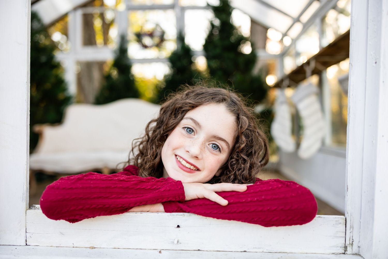Someone in a burgundy sweater leans on a white railing with curly hair and a bright smile outdoors.