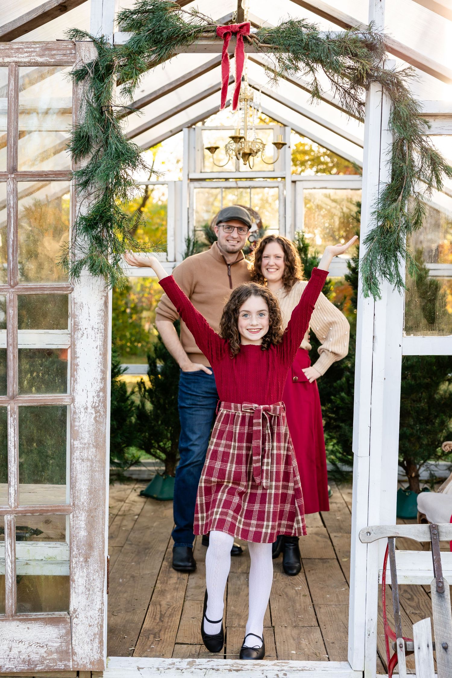 A series of holiday photos taken in a greenhouse decorated with red ribbons and evergreen garlands.