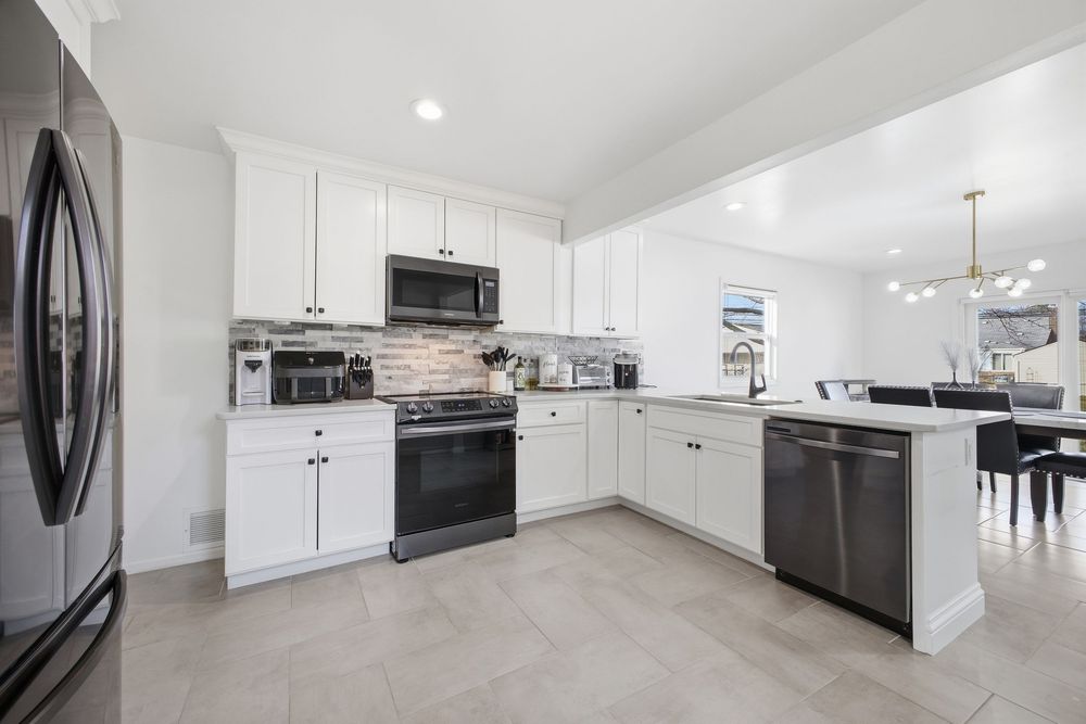 Bright white kitchen with stainless appliances, stone backsplash, and open view to dining room.