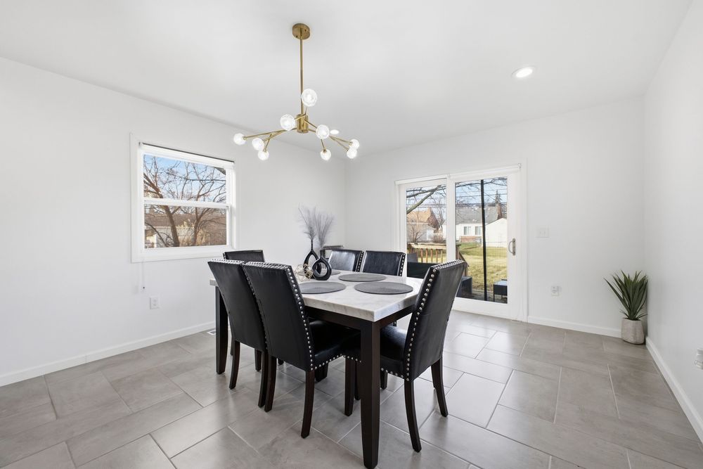 Dining room with modern gold chandelier, dark table, six chairs, and large sliding glass door.