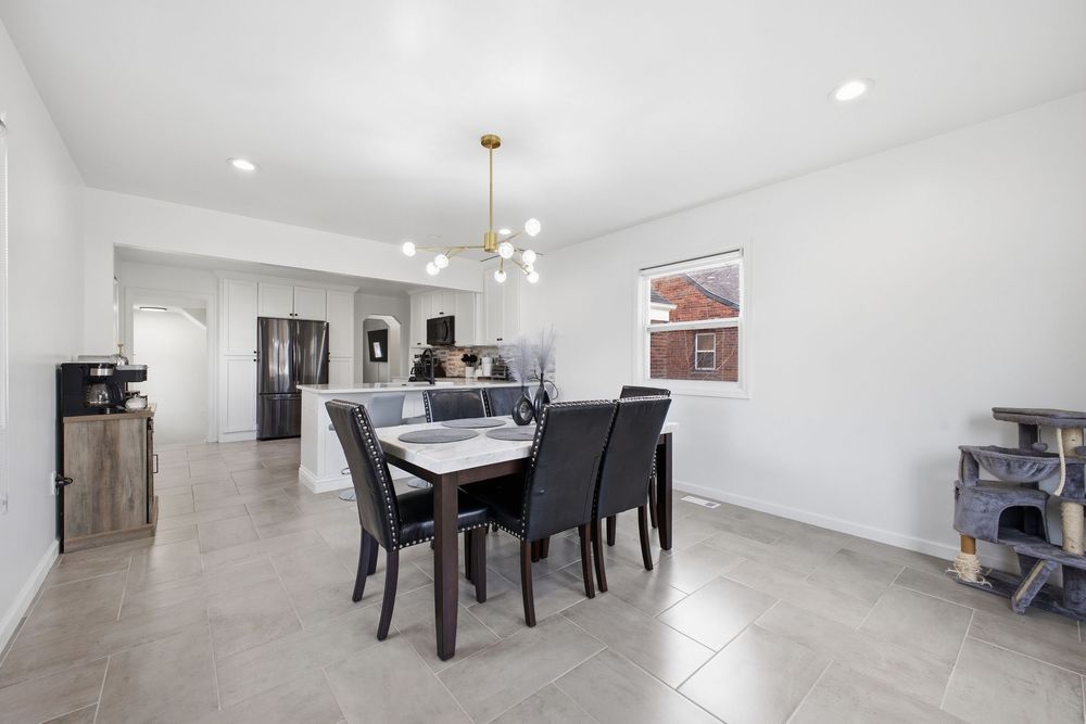 Open dining area with gold chandelier, dark table set, tile floors, and view into kitchen.