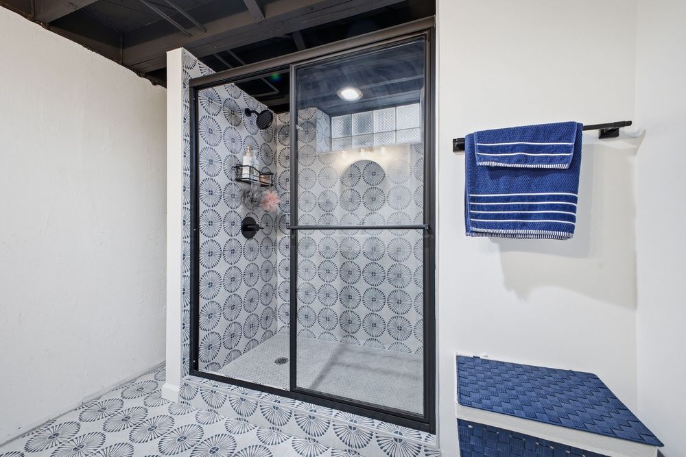 Basement bathroom with patterned tile shower, glass door, and decorative blue towels.