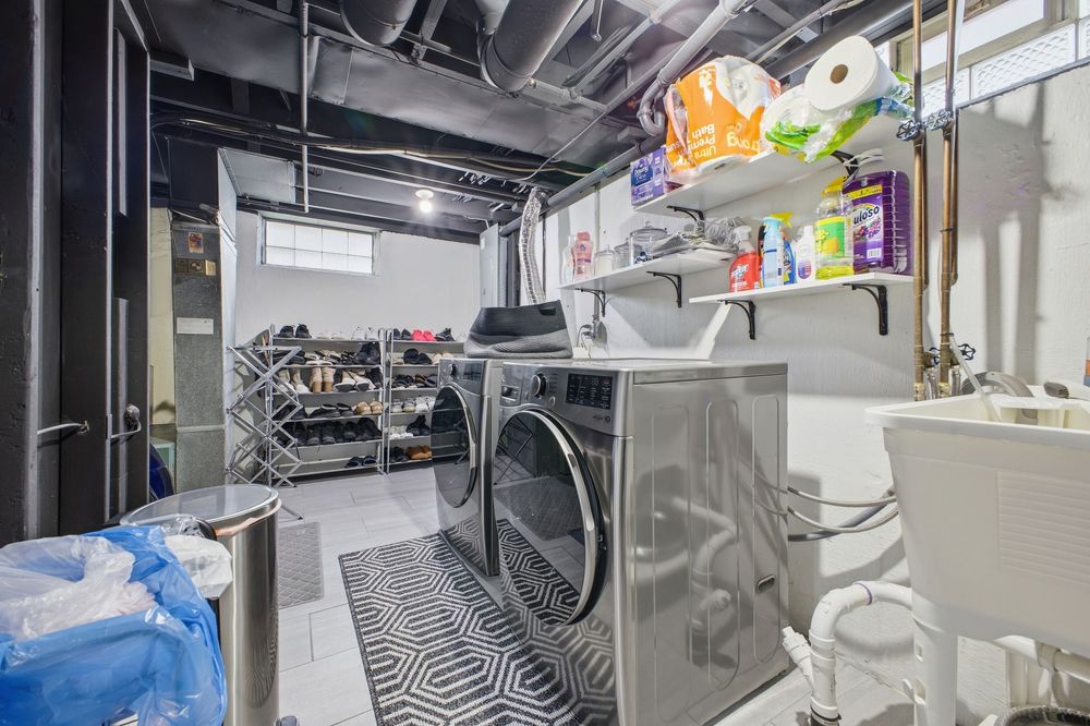 Unfinished basement laundry area with front-load washer and dryer and utility sink.