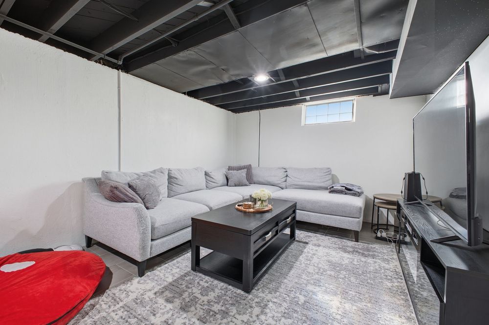Finished basement living room with gray sectional sofa, dark coffee table, and exposed black ceiling.
