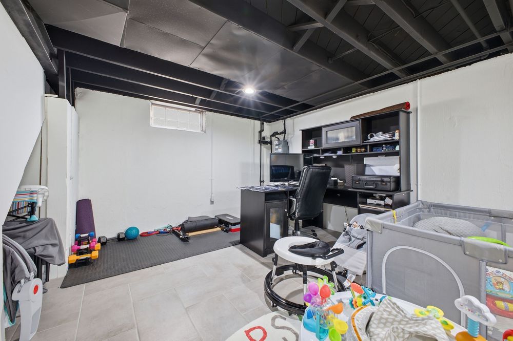 Basement home office and gym space with black shelving unit, desk, exercise equipment, and painted black ceiling.