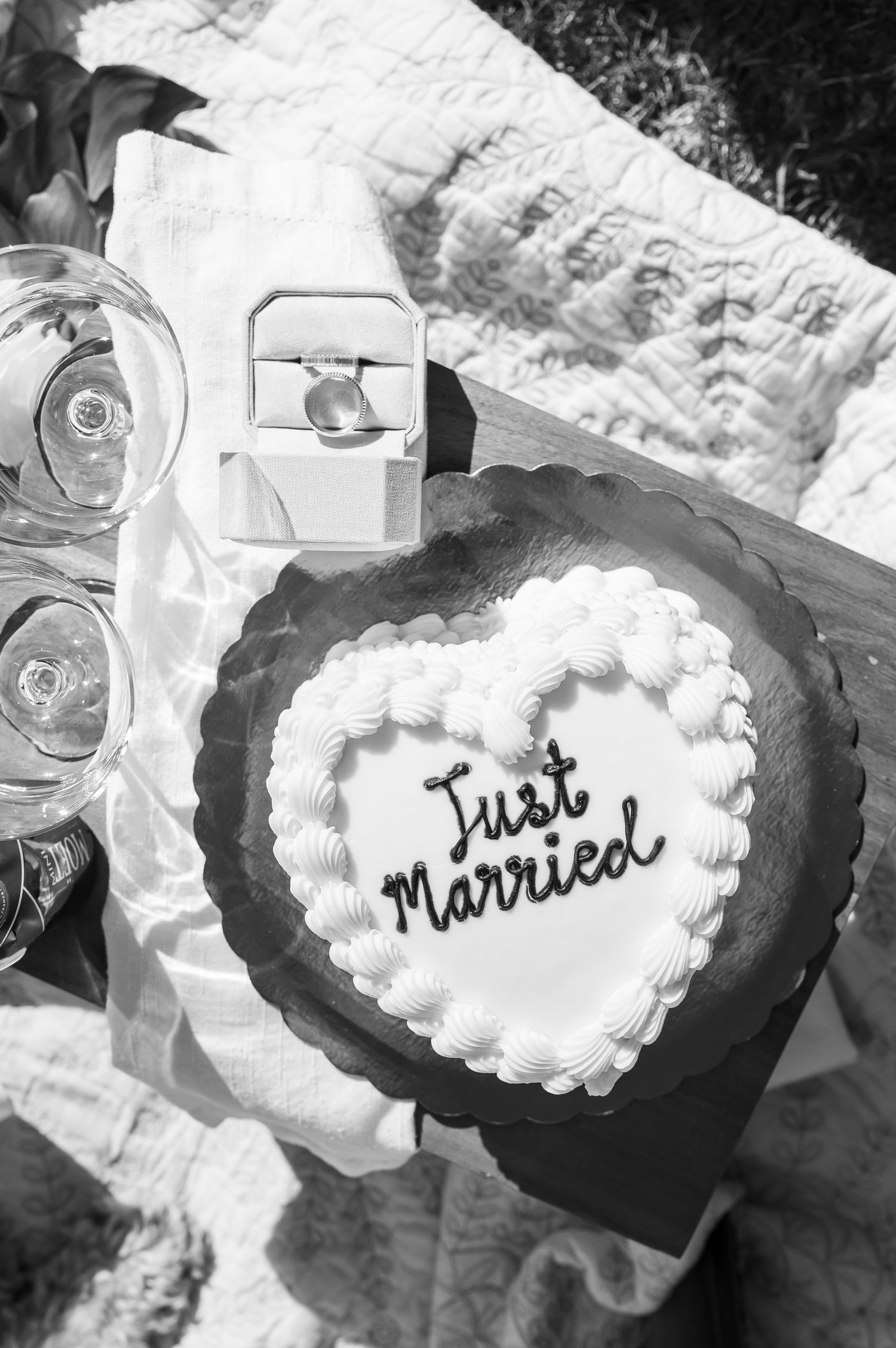 Black and white photo of a heart-shaped Just Married wedding cake beside champagne glasses and a ring box for Colorado Elopement