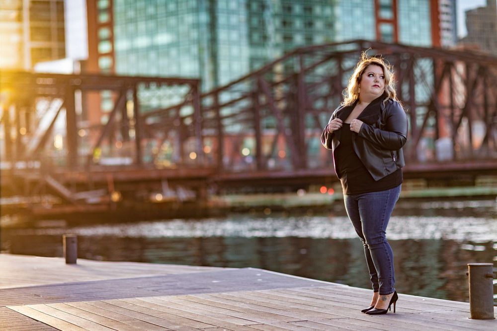 Maternity portrait on wooden deck with urban bridge and buildings in background.