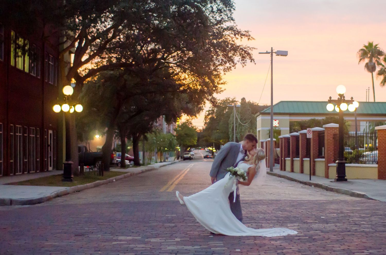 Couple sharing romantic dip kiss on brick street at sunset during outdoor wedding photo session.