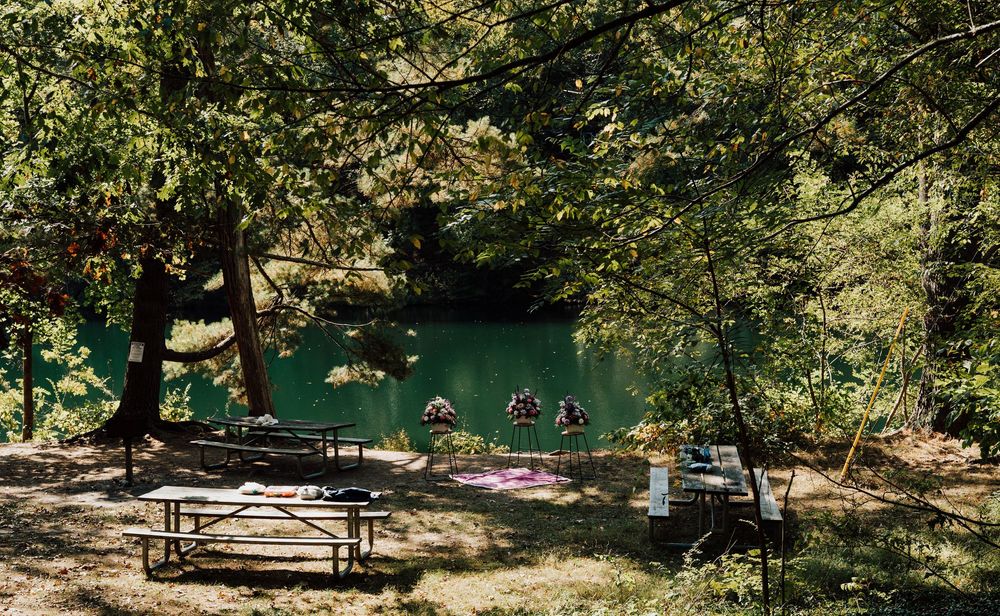 Shaded picnic area with wooden benches beside fuller lake in central pa surrounded by lush trees.