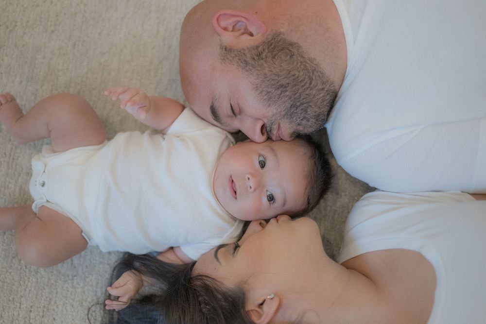 Overhead view of bald father and dark-haired mother cuddling their alert newborn baby.