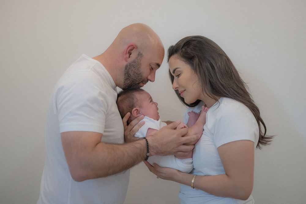 New parents tenderly hold their newborn baby together, touching foreheads in an intimate family moment.