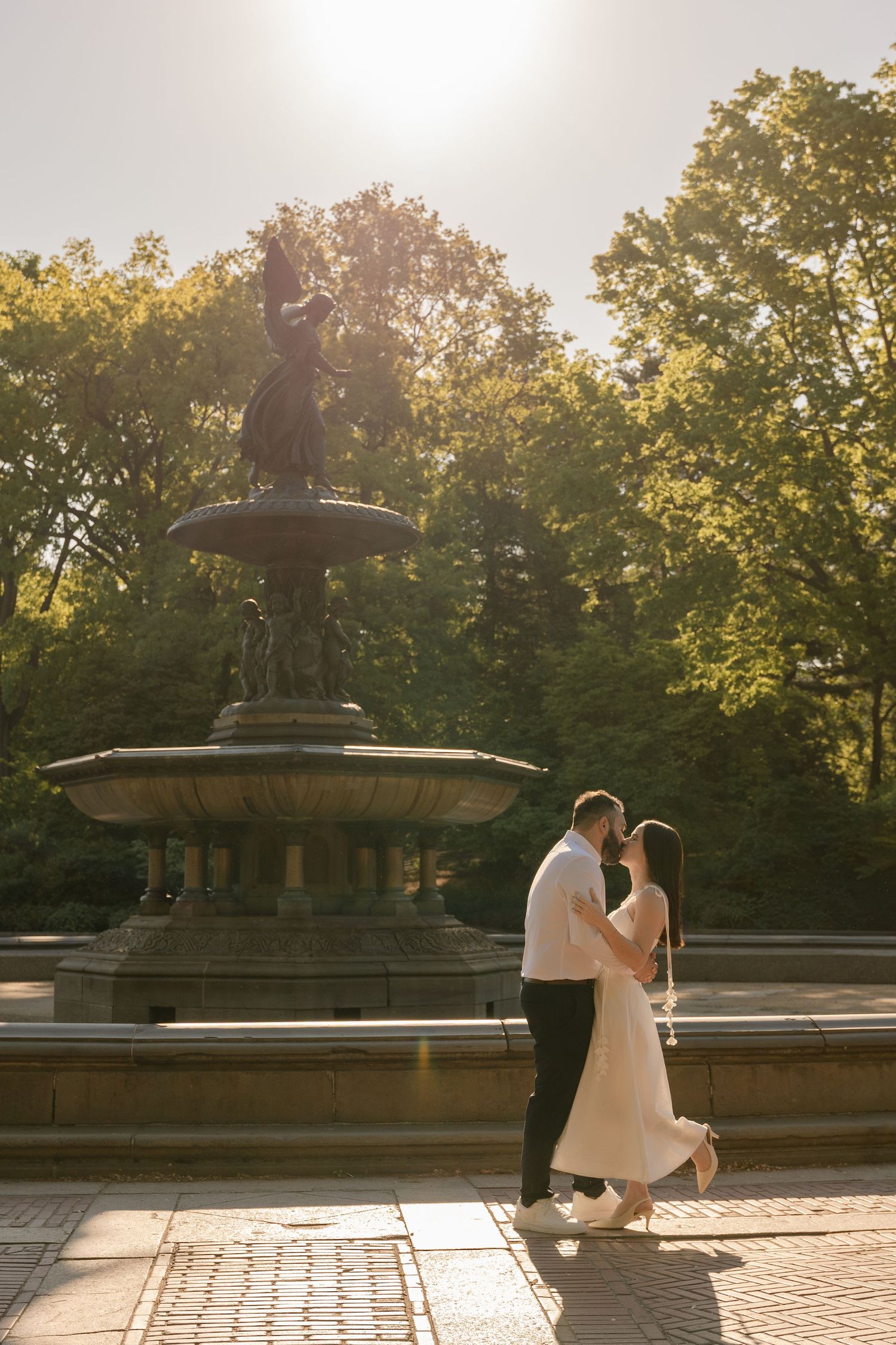 Couple sharing a romantic kiss in front of Bethesda Fountain in Central Park, NYC, bathed in golden sunlight.