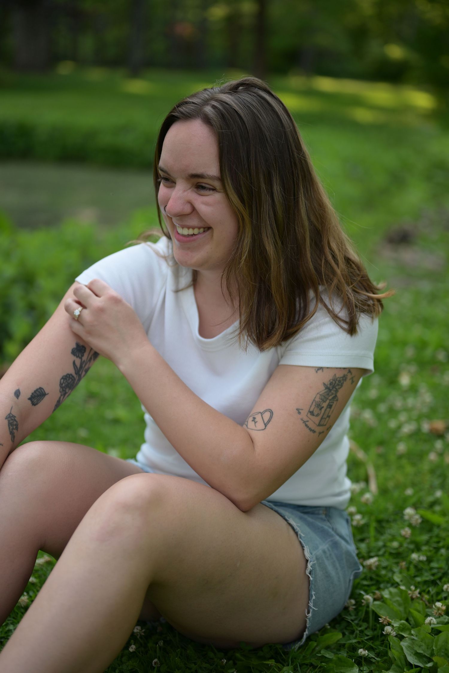 Middle-aged woman in white tank top smiling outdoors in a sunny park setting with green trees in background.