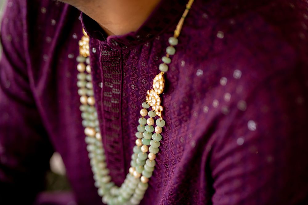 Close-up of a person wearing a purple embroidered kurta with a multi-strand jade beaded necklace featuring a gold pendant.