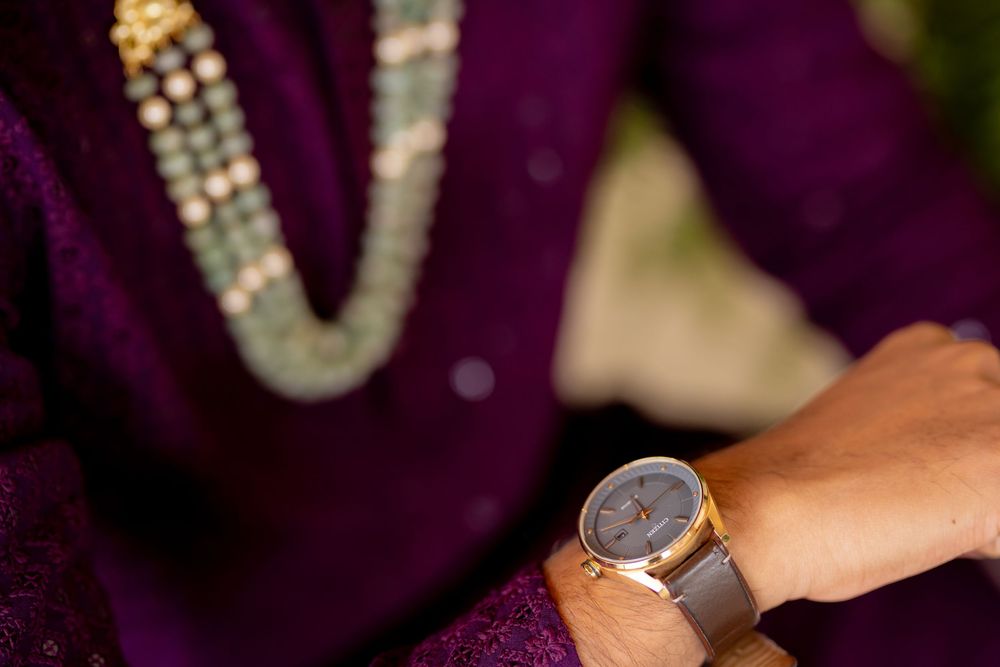 Person wearing purple outfit with beaded necklace and gold wristwatch, elegant fashion accessories close-up.