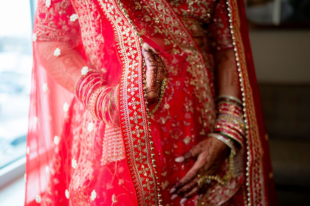 Close-up of Indian bride in red and gold embroidered lehenga with mehndi hands and bangles.