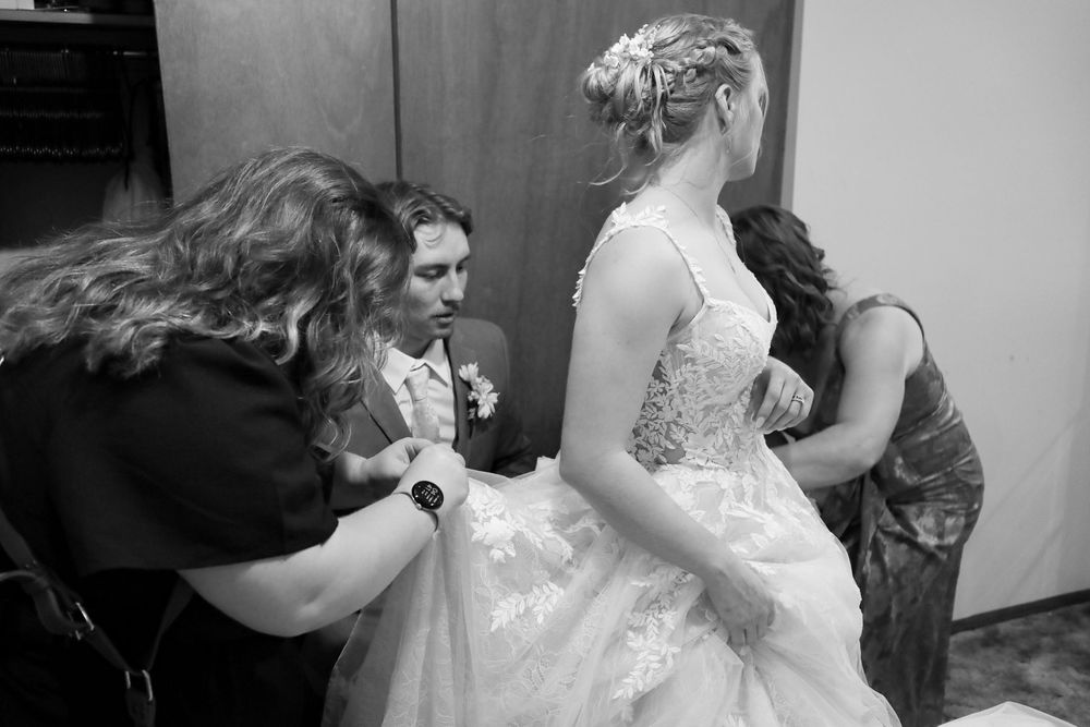 Black and white photo of a bride in a white lace gown being helped by two women before her wedding ceremony.