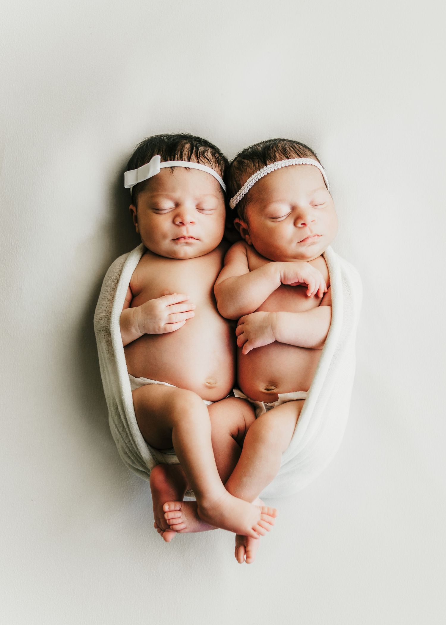 Newborn twins lying together on a white blanket