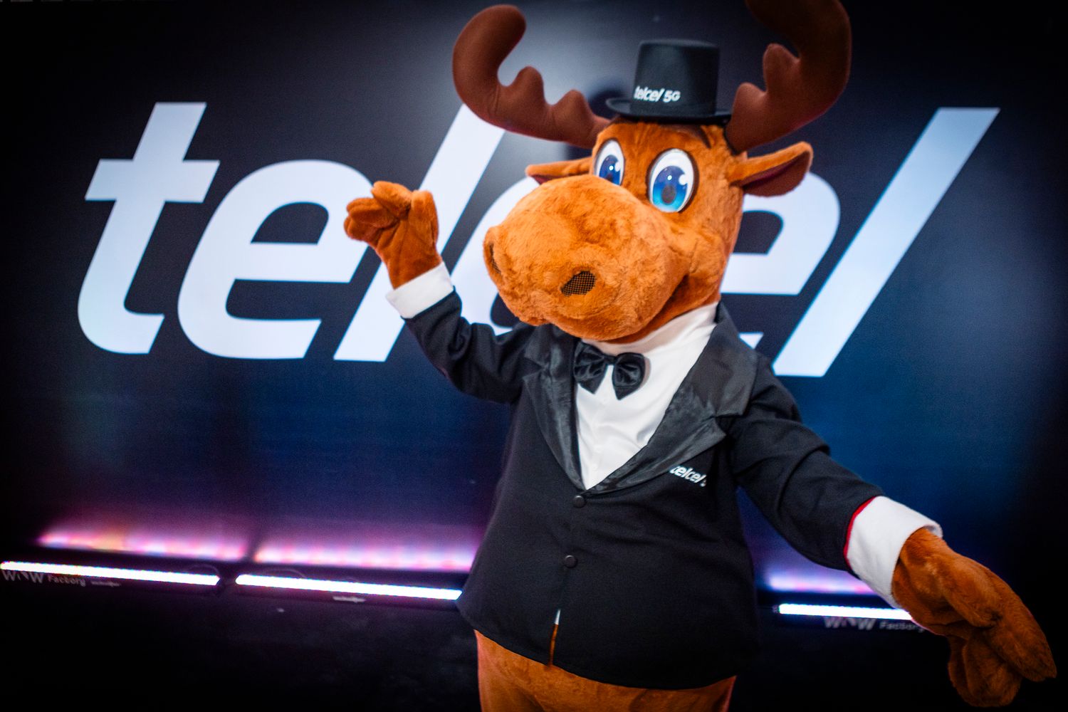 Tele2 mascot moose in tuxedo and top hat poses in front of branded Tele2 logo backdrop.